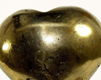 May include: A heart-shaped polished pyrite stone with a golden color. The stone is on a clear plastic stand.