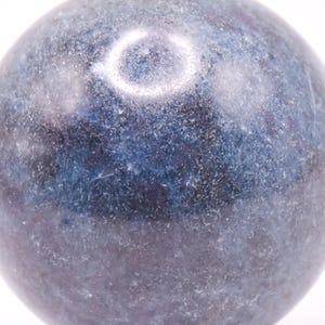 May include: A polished, spherical gemstone in shades of blue and gray. The orb has a smooth, reflective surface with subtle variations in color and texture. The gemstone is mounted on a small, silver-colored base.