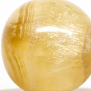 May include: A golden-yellow sphere with a polished, translucent appearance. The orb has subtle, swirling patterns and a smooth surface. The sphere is mounted on a silver-colored base, creating a decorative accent piece.