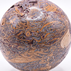 May include: A spherical decorative object with a textured surface. The sphere features a mix of brown, tan, and dark purple hues with intricate patterns. The patterns appear to be fossilized or organic in nature, adding to its unique aesthetic.