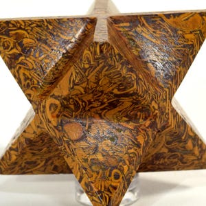 May include: A six-pointed star-shaped sculpture with a unique pattern of brown and dark brown swirls. The geometric art piece is made of a solid material and sits on a clear stand, showcasing its intricate design.