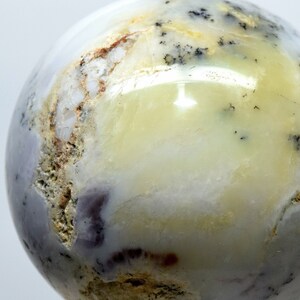 May include: A polished, white, yellow, and purple agate sphere with black dendritic inclusions. The sphere is approximately 2 inches in diameter.