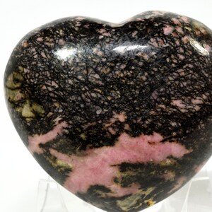 May include: A heart-shaped polished pink and black rhodochrosite stone with black dendritic inclusions.