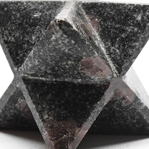 Op de afbeelding: Een zwarte stervormige kristal met een ruw, getextureerd oppervlak. De kristal heeft een licht iriserende glans en is gemaakt van een donker, ondoorzichtig materiaal.