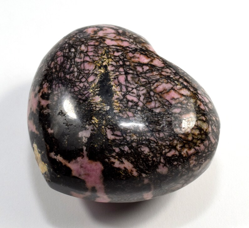 May include: A heart-shaped polished stone with a pink and black pattern. The stone has a smooth, glossy finish and is a natural mineral.