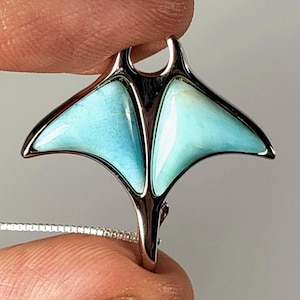 May include: A silver pendant shaped like a manta ray with blue and green gemstone accents.