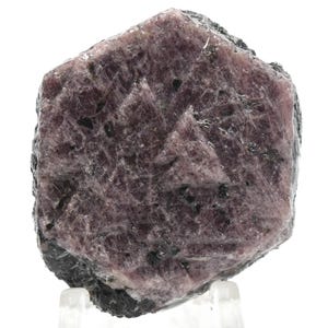 Può includere: Un grande cristallo di rubino rosa grezzo con inclusioni nere. Il cristallo è di forma esagonale e ha una finitura opaca.