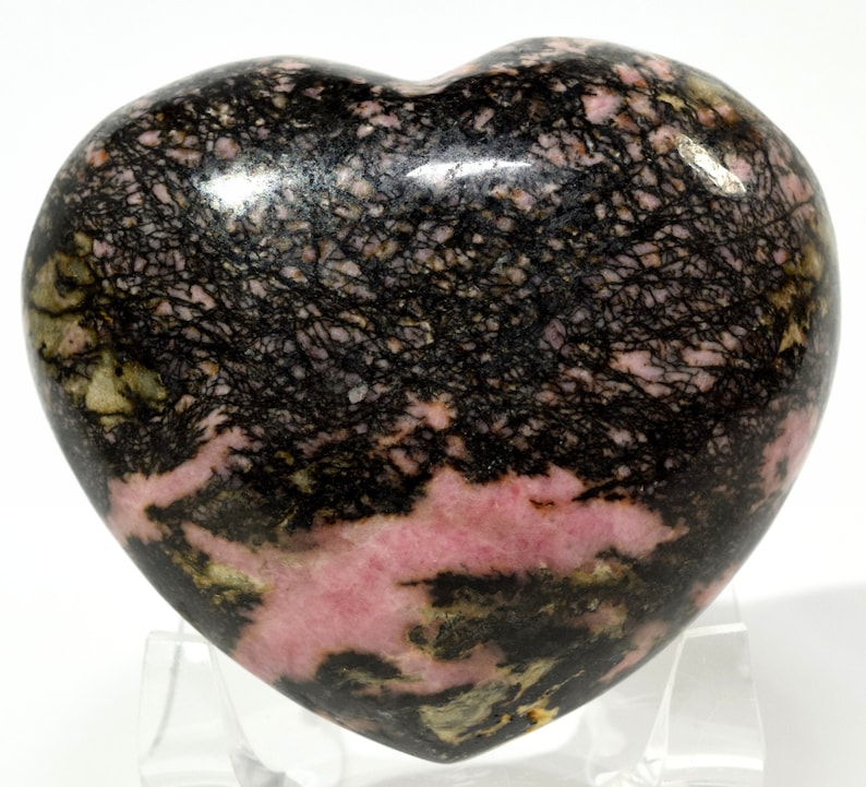 May include: A heart-shaped polished pink and black rhodochrosite stone with black dendritic inclusions.