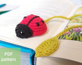 May include: A crocheted ladybug bookmark with black eyes and a green leaf tail. The bookmark is on a book with the text "PDF pattern" on the cover.