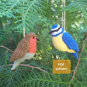 May include: Two crocheted bird ornaments hanging from strings. One bird has brown wings, a red chest, and a light gray belly. The other bird has a blue head with a white stripe, a yellow chest, and blue wings. A yellow box contains the text PDF pattern.