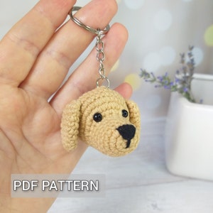 Peut inclure: Porte-clés en crochet en forme de chien avec un corps beige, un nez noir et des yeux noirs. Le porte-clés est attaché à un anneau de clé argenté.