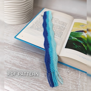 Könnte beinhalten: Ein blaues und türkisfarbenes Häkel-Lesezeichen mit einem wellenförmigen Design und Fransen. Das Lesezeichen liegt auf einem geöffneten Buch. Der Text "PDF PATTERN" ist in der linken unteren Ecke des Bildes sichtbar.