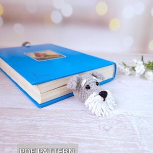 Könnte beinhalten: Handgefertigter Häkel-Lesezeichen in Form eines Schnauzer-Hundes, mit grauen und weißen Garndetails. Das Lesezeichen befindet sich in einem blauen Buch. Der Text "PDF PATTERN" ist unten im Bild zu sehen.