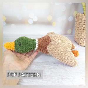 May include: A handmade crochet duck toy in shades of green, brown, tan, and yellow. The duck has a green head, brown body, and tan wings. The text "PDF PATTERN" is visible.