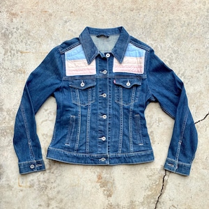 May include: A blue denim jacket with a pink and blue quilted patch on the back of the collar.