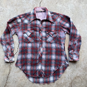 May include: A red, black, and white plaid flannel shirt with a pointed collar and long sleeves. The shirt has two chest pockets with button closures and a curved hem.