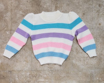 May include: A white striped jumper with blue, purple and pink stripes. The jumper has a crew neck and long sleeves.
