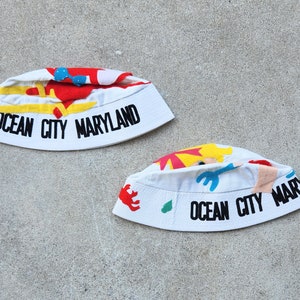 May include: Two white bucket hats with colorful patches and the text "Ocean City Maryland" on the brim.
