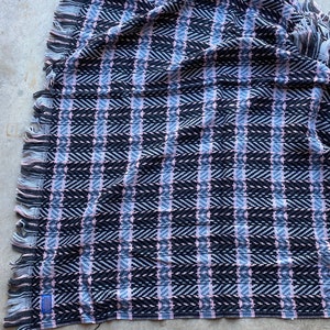 Może przedstawiać: Wełniany koc tkany w kolorze czarnym, r&oacute;żowym i szarym z frędzlami na brzegach.