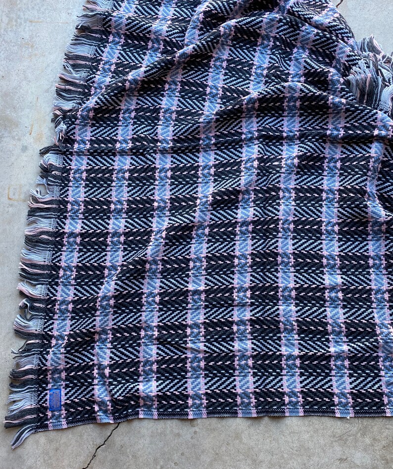 Może przedstawiać: Wełniany koc tkany w kolorze czarnym, r&oacute;żowym i szarym z frędzlami na brzegach.