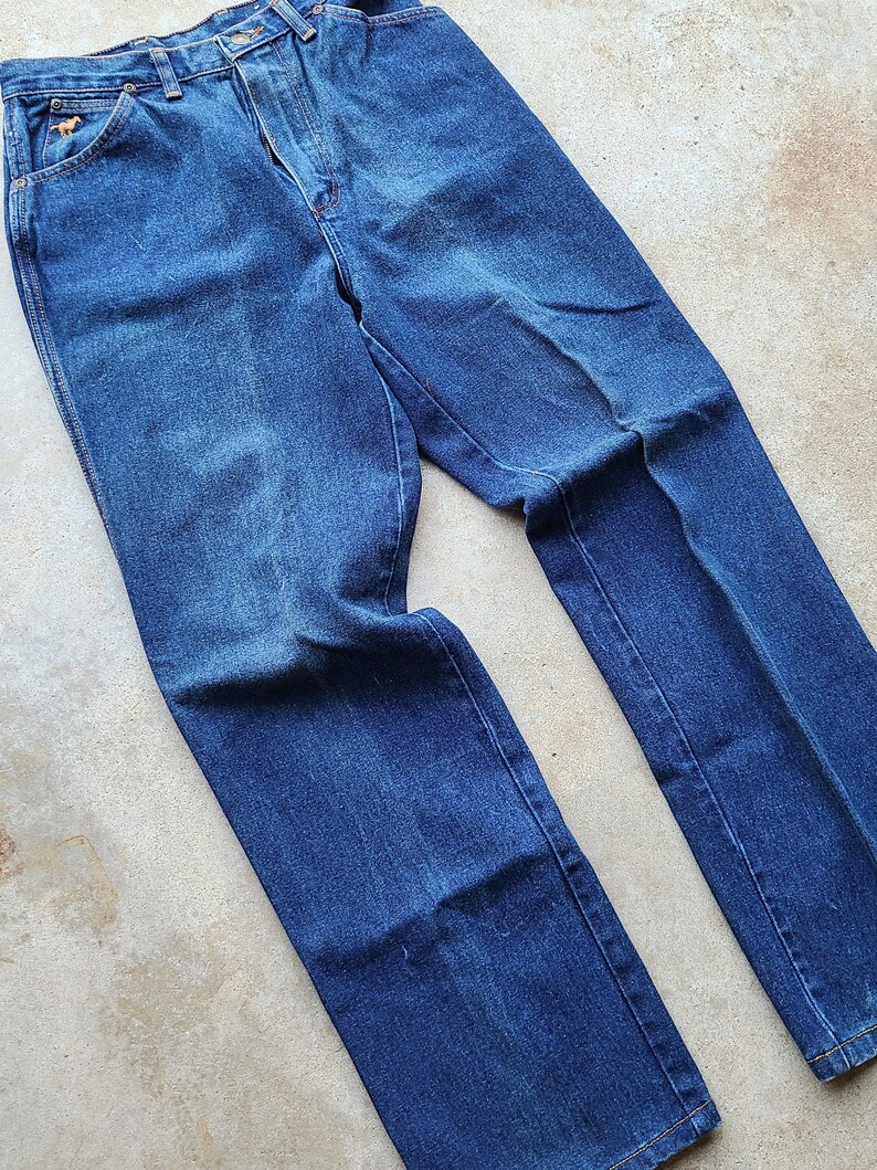 Puede incluir: Un par de pantalones vaqueros azules de denim con corte recto. Los vaqueros tienen un dise&ntilde;o cl&aacute;sico de cinco bolsillos y cierre de bot&oacute;n.
