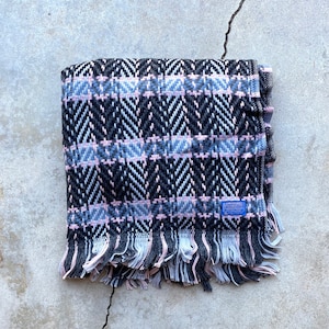 Może przedstawiać: Czarny, r&oacute;żowy i niebieski pled z frędzlami. Pled ma tkane logo z napisem "Pendleton".