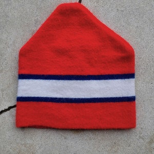 May include: Red knit beanie with a white and navy blue stripe.
