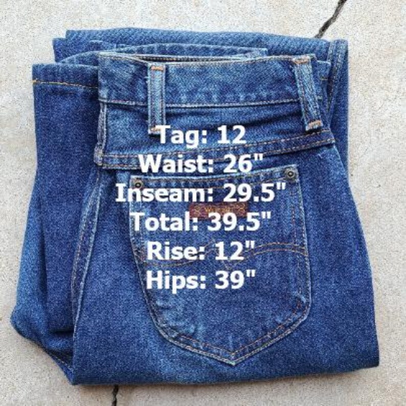 Puede incluir: Un par de pantalones vaqueros azules de mezclilla con una etiqueta de cuero marr&oacute;n. Los pantalones tienen una altura de tiro de 12 pulgadas, una cintura de 26 pulgadas, una entrepierna de 29,5 pulgadas y una cadera de 39 pulgadas. La etiqueta dice "Tag: 12".