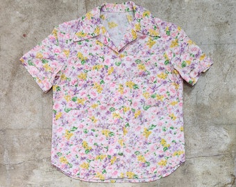 May include: A short-sleeved button-up shirt with a floral print in shades of pink, yellow, and purple.
