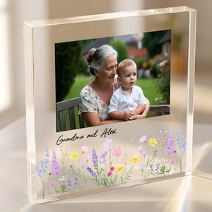 May include: A clear acrylic photo block with a printed photograph of a woman and a baby. The block features a floral design at the bottom and the text "Grandma and Alex".