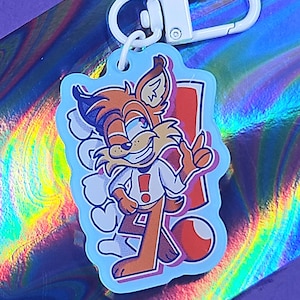 May include: A light blue keyring featuring a cartoon fox character with orange and white accents. The fox is smiling and giving a thumbs up. The keyring has a white clasp.