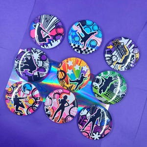 May include: A collection of eight circular pin-back buttons featuring vibrant, multi-colored graphic designs. Each button displays a black silhouette of a person in a dynamic pose set against abstract patterns, geometric shapes, and bright color palettes.