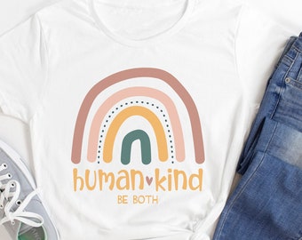 May include: White t-shirt with a rainbow graphic and the words "HUMAN KIND BE BOTH" in orange. The shirt is paired with blue jeans and gray sneakers with white laces. A casual, everyday outfit.