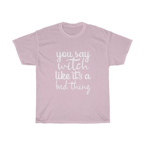 May include: A light pink t-shirt with the phrase "you say witch like it's a bad thing" in white script. The shirt is a crew neck style and appears to be made of a soft material.