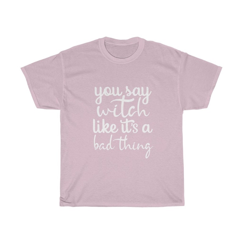 May include: A light pink t-shirt with the phrase "you say witch like it's a bad thing" in white script. The shirt is a crew neck style and appears to be made of a soft material.