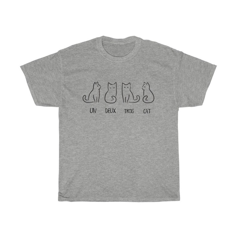 May include: A heather gray t-shirt featuring a minimalist design of four black cat illustrations. The text "UN DEUX TROIS CAT" is printed below the cats. The shirt is made of a soft, comfortable material.