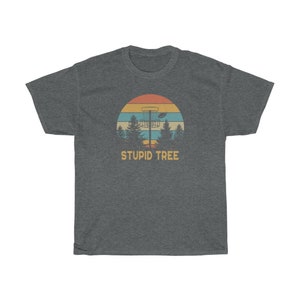 Pode incluir: T-shirt cinzento escuro com um design retro de disc golf. O gr&aacute;fico inclui um cesto de disc golf, &aacute;rvores e um p&ocirc;r do sol. O texto "STUPID TREE" est&aacute; por baixo. Uma t-shirt casual para jogadores de disc golf.