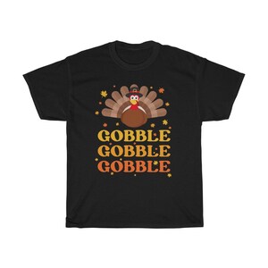 May include: Black t-shirt featuring a Thanksgiving turkey illustration with a pilgrim hat and autumn leaves. The words "GOBBLE GOBBLE GOBBLE" are printed in yellow and orange below the turkey design.