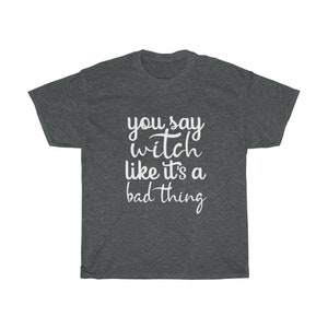May include: Dark gray t-shirt with the white text "you say witch like it's a bad thing". The shirt has a crew neck and short sleeves. The text is in a handwritten style font.