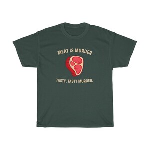 Op de afbeelding: Donkergroen t-shirt met de tekst "MEAT IS MURDER" boven een cartoon steak illustratie. Onder de illustratie staat de tekst "TASTY, TASTY MURDER."