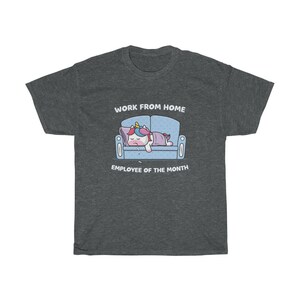 K&ouml;nnte beinhalten: Dunkelgraues T-Shirt mit einem Cartoon-Einhorn, das auf einem blauen Sofa schl&auml;ft. Der Text "WORK FROM HOME EMPLOYEE OF THE MONTH" ist oberhalb und unterhalb der Einhorn-Illustration aufgedruckt. Das Shirt ist aus weichem Material.