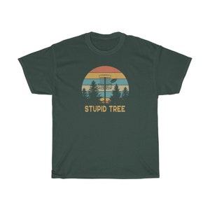 Pode incluir: T-shirt verde escuro com um design retr&ocirc; com uma cesta de disc golf, &aacute;rvores e um p&ocirc;r do sol. O texto "STUPID TREE" est&aacute; abaixo do gr&aacute;fico. A camisa &eacute; feita de um material macio e confort&aacute;vel.