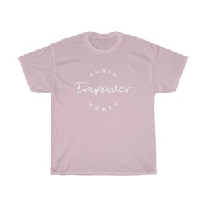May include: A light pink t-shirt with the words "Women Empower Women" in a white, circular design. The shirt is made of a soft material and has a classic crew neck.
