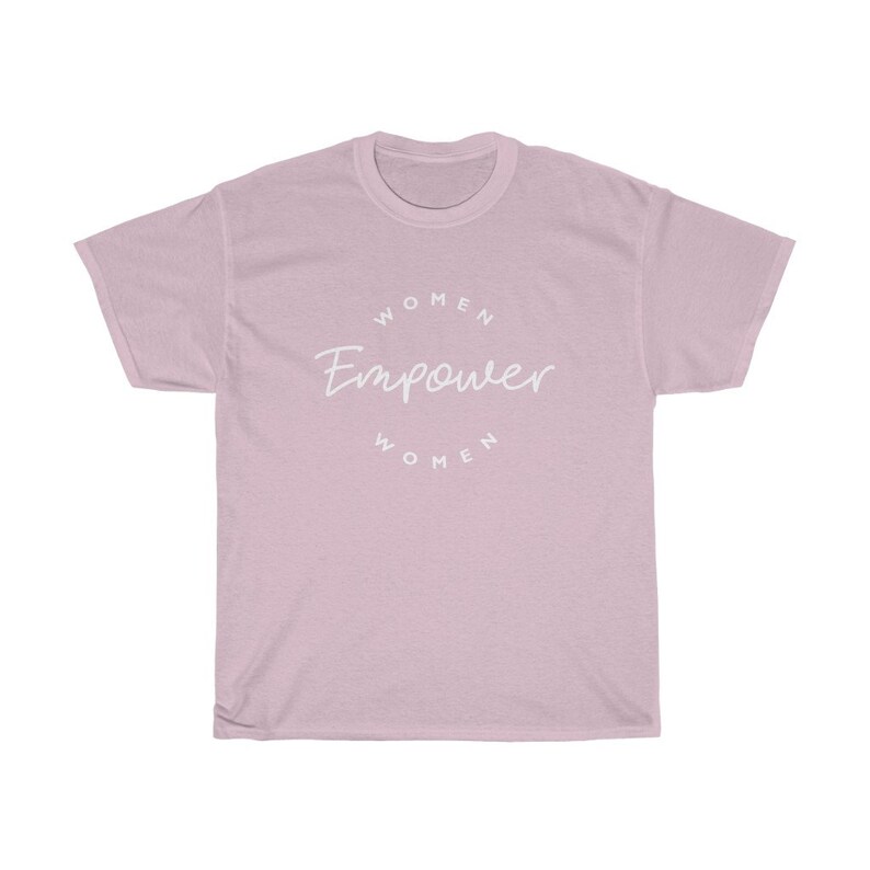 May include: A light pink t-shirt with the words "Women Empower Women" in a white, circular design. The shirt is made of a soft material and has a classic crew neck.