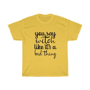May include: Mustard yellow t-shirt with the phrase "you say witch like it's a bad thing" in black script. The shirt is a crew neck style and appears to be made of a soft material. The text is centered on the front of the shirt.