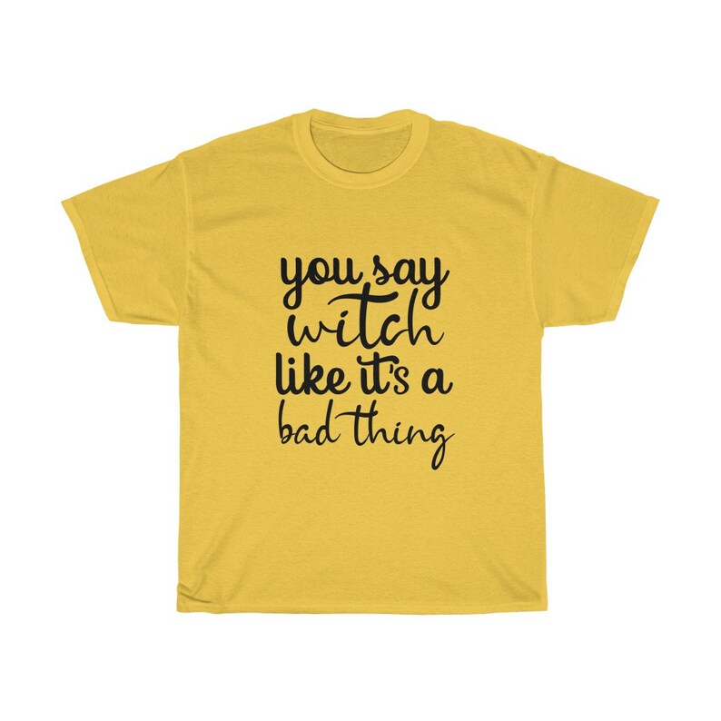 May include: Mustard yellow t-shirt with the phrase "you say witch like it's a bad thing" in black script. The shirt is a crew neck style and appears to be made of a soft material. The text is centered on the front of the shirt.