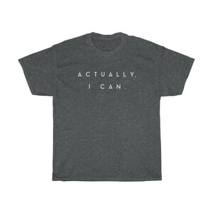 Op de afbeelding: Donkergrijs t-shirt met de tekst "ACTUALLY, I CAN." in het wit. Het shirt heeft een ronde hals en korte mouwen. De stof lijkt een zacht, comfortabel materiaal te zijn.
