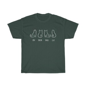 May include: Dark green t-shirt featuring a white line drawing of four cats in different poses. The text "UN DEUX TROIS CAT" is printed below the cats. The shirt is made of a soft, comfortable material.
