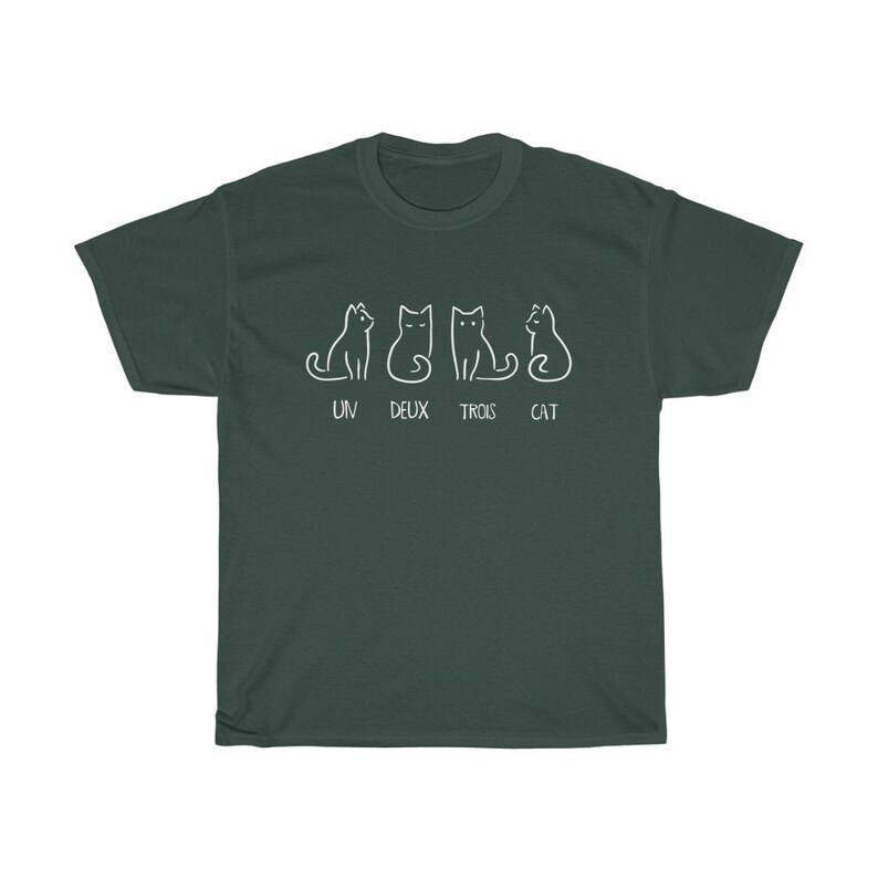 May include: Dark green t-shirt featuring a white line drawing of four cats in different poses. The text "UN DEUX TROIS CAT" is printed below the cats. The shirt is made of a soft, comfortable material.