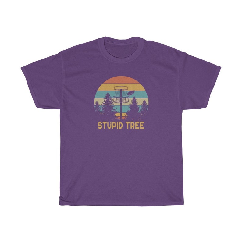 Pode incluir: Camiseta roxa com um design retr&ocirc; com uma cesta de disc golf, &aacute;rvores e um p&ocirc;r do sol. O texto "STUPID TREE" &eacute; impresso abaixo. Uma camiseta casual para os entusiastas do disc golf.